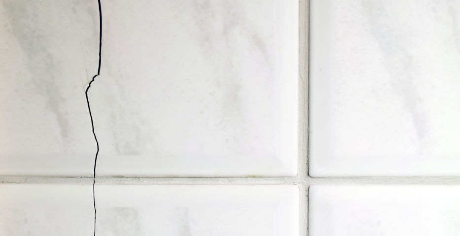 Cracked tiles on the bathroom wall need repair. Possible sign of water damage. Horizontal image of building problems concept.